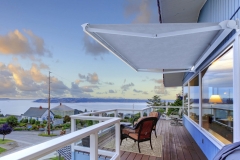 Large balcony of blue house with chairs and water view.